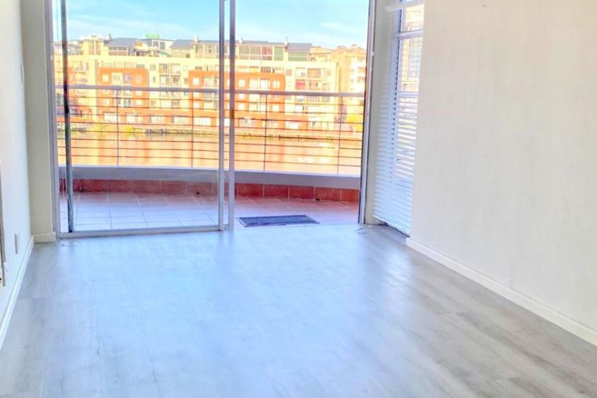 Bright and spacious empty living area featuring modern laminate flooring and large sliding glass doors leading to a private balcony with urban views.
