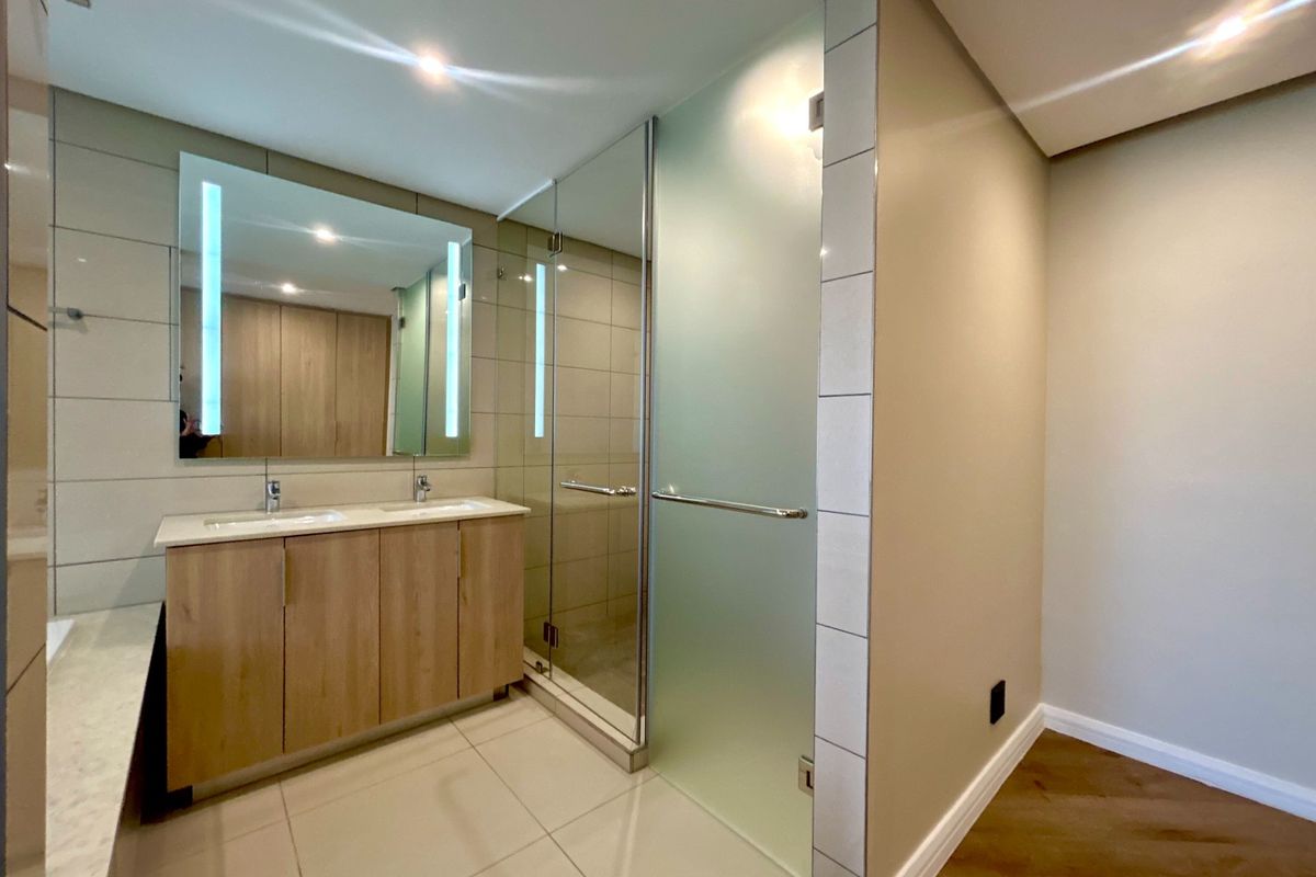 Modern bathroom featuring a double vanity with integrated LED mirror, glass shower enclosure, and neutral tiled finishes.
