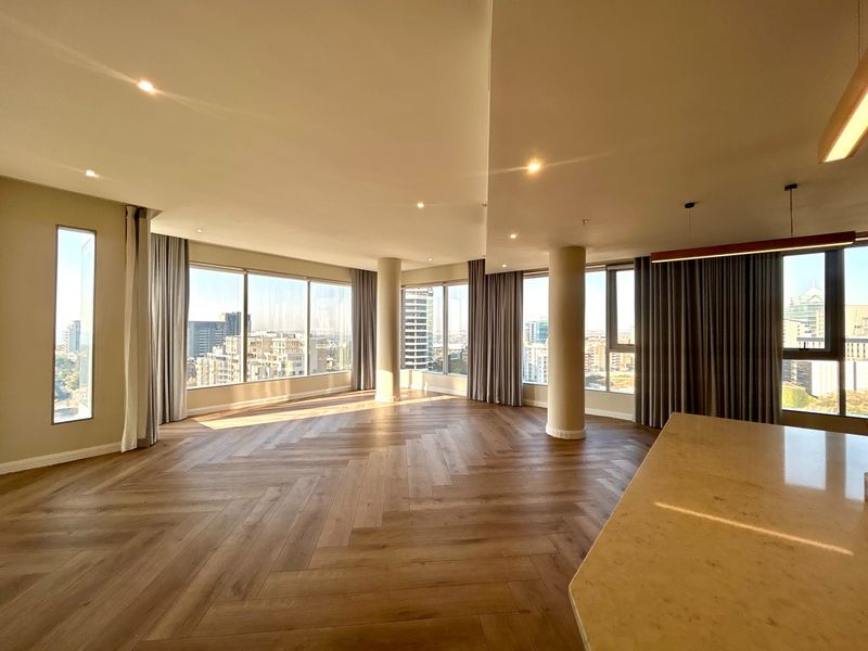 Spacious open-plan living area featuring herringbone timber flooring, floor-to-ceiling windows with city views, and a modern stone kitchen island.
