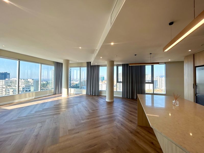Spacious open-plan living area featuring herringbone timber flooring, floor-to-ceiling windows with city views, and a modern kitchen island with stone countertops.