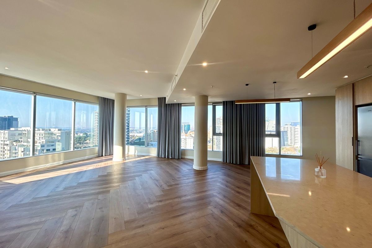 Spacious open-plan living area featuring herringbone timber flooring, floor-to-ceiling windows with city views, and a modern kitchen island with stone countertops.