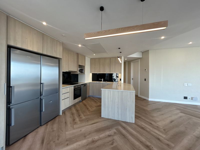 Modern kitchen featuring light wood cabinetry, a central island, integrated appliances, and stylish herringbone flooring in an open-plan layout.