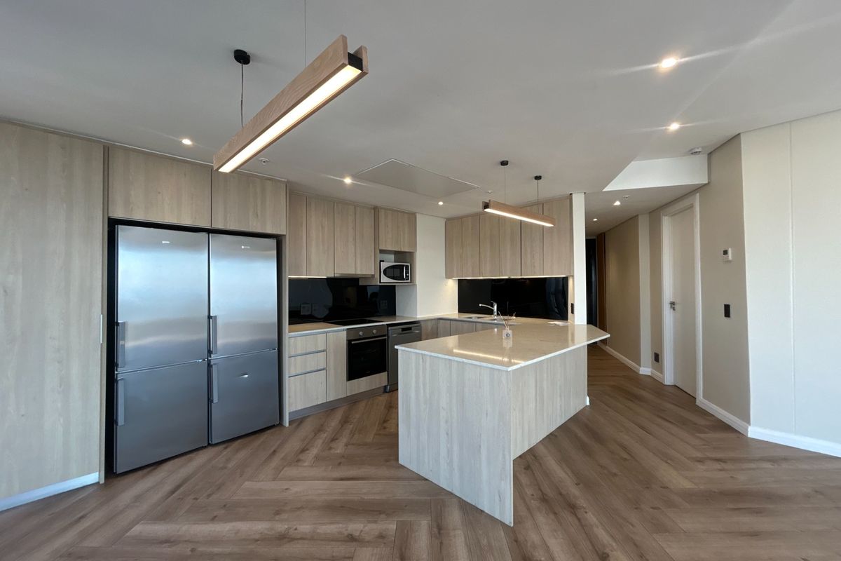 Modern kitchen featuring light wood cabinetry, stone countertops, a central island, integrated appliances, and stylish herringbone flooring in an open-plan layout.
