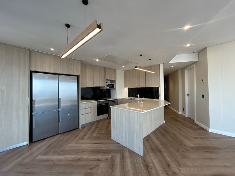 Modern kitchen featuring light wood cabinetry, stone countertops, a central island, integrated appliances, and stylish herringbone flooring in an open-plan layout.
