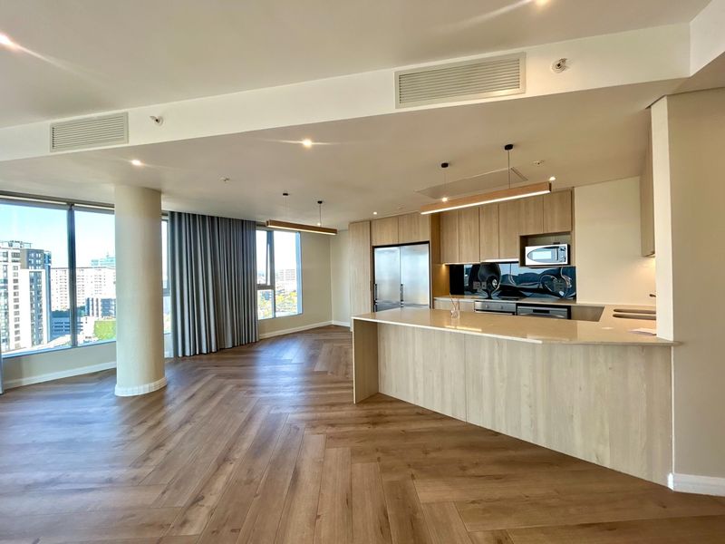 Modern open-plan living area featuring herringbone timber flooring, a sleek kitchen with stone island, integrated appliances, and expansive floor-to-ceiling windows with city views.