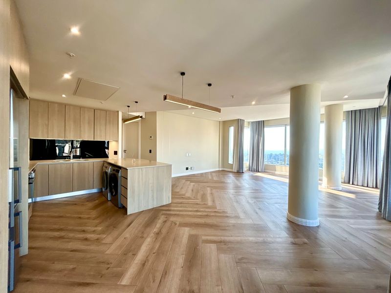 Spacious open-plan living area featuring modern light wood cabinetry, a kitchen island, herringbone flooring, and floor-to-ceiling windows with expansive city views.