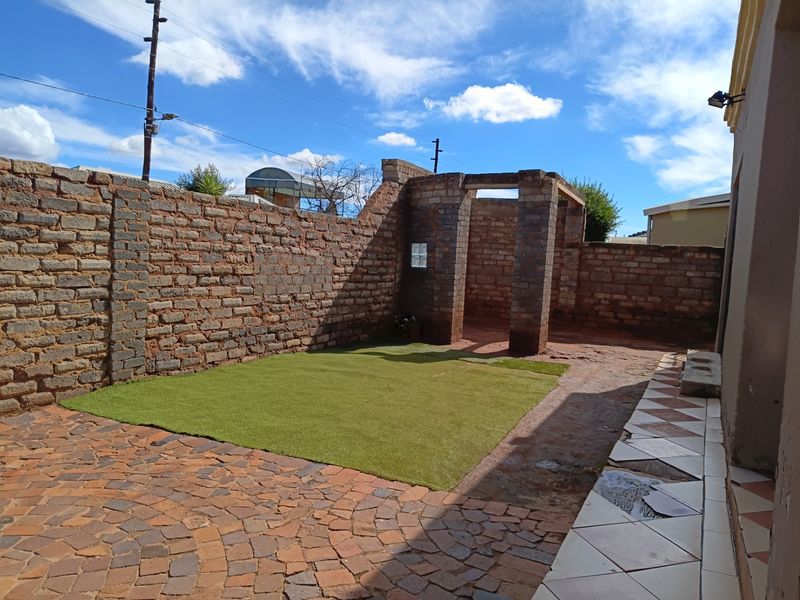 Rear courtyard area featuring a paved patio, artificial grass section, and an unfinished brick structure, offering potential for outdoor landscaping and entertainment space development.