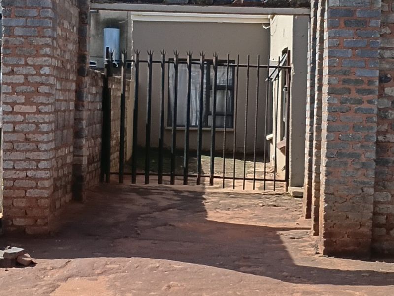 Front entrance view featuring a brick gate structure, metal security gate, and paved driveway leading to the property facade.