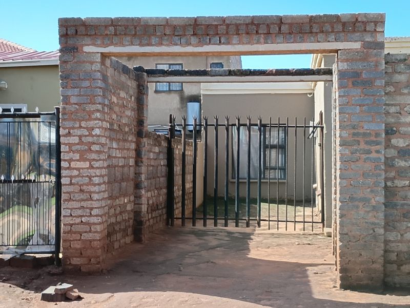 Front entrance area featuring a brick boundary wall and metal security gate leading to the property driveway.