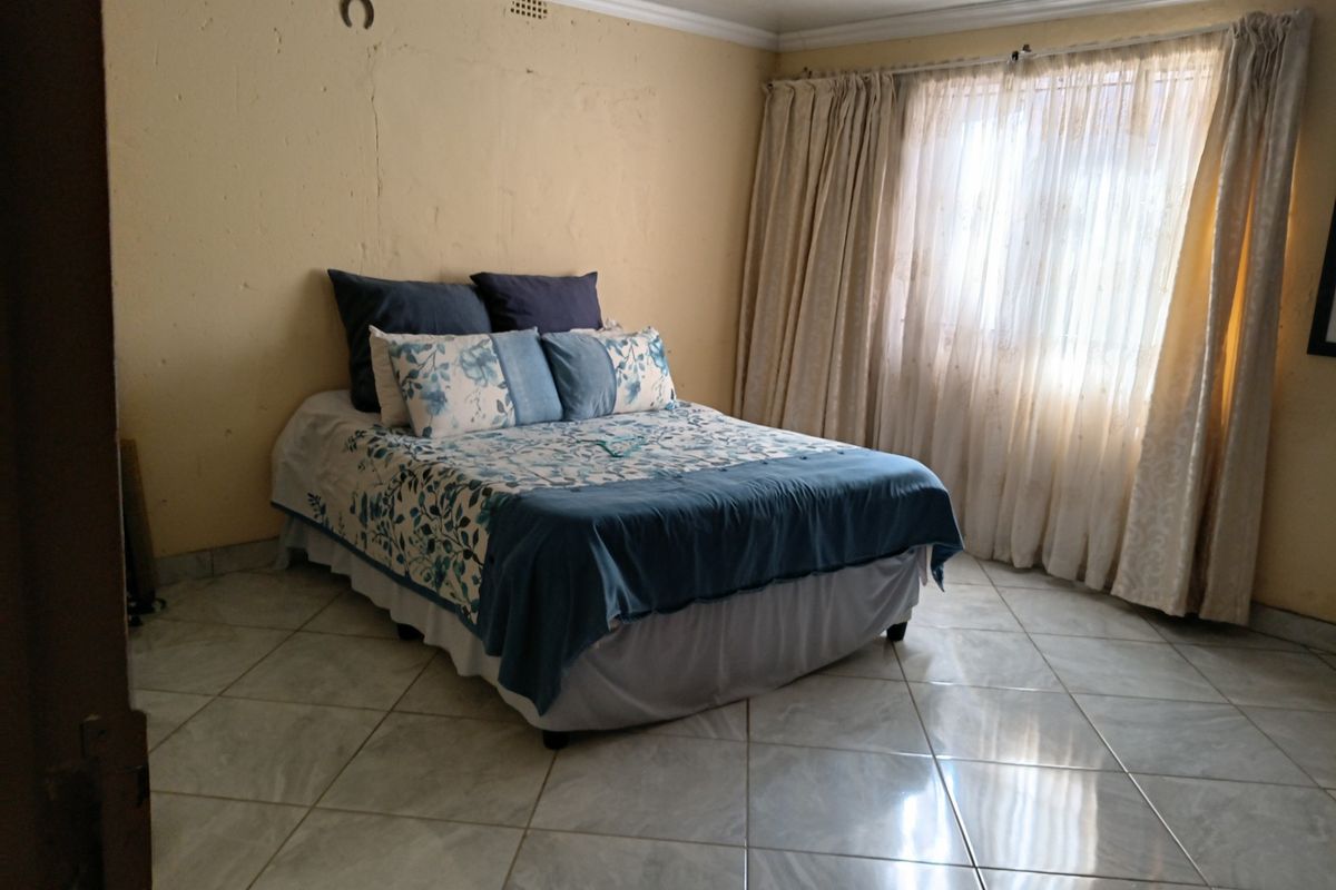 A bedroom featuring tiled flooring, crown molding, and large windows with curtain rails. The walls show signs of wear and require cosmetic attention.