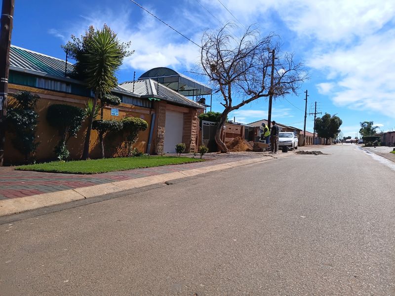 A street-level view of the property frontage showing the boundary wall, electric fencing, and paved sidewalk area.