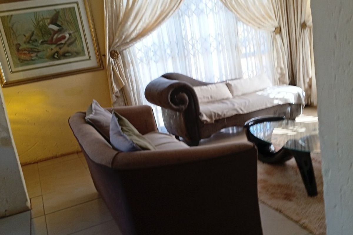 A living room area featuring tiled flooring and large windows with security gates, offering a dated interior space ready for modernization.
