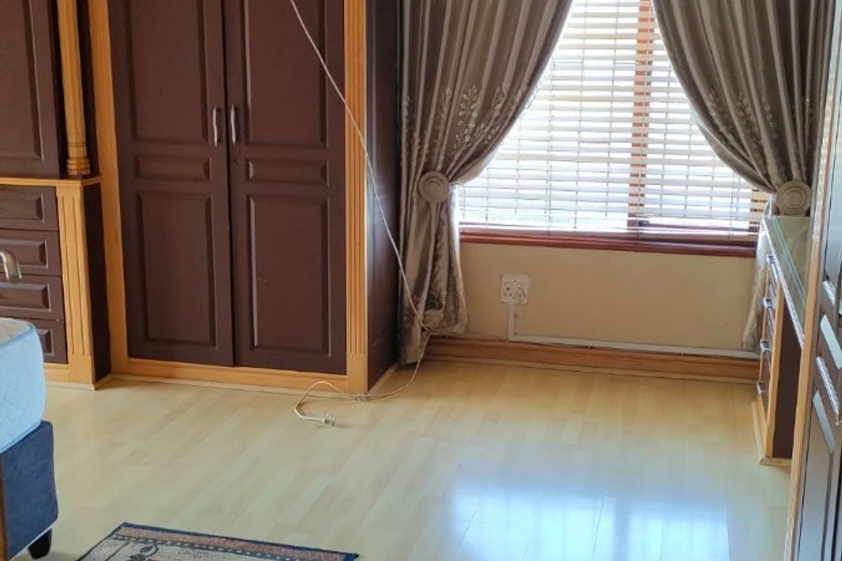 Bedroom featuring extensive built-in dark wood cabinetry, light laminate flooring, and large window with integrated blinds.