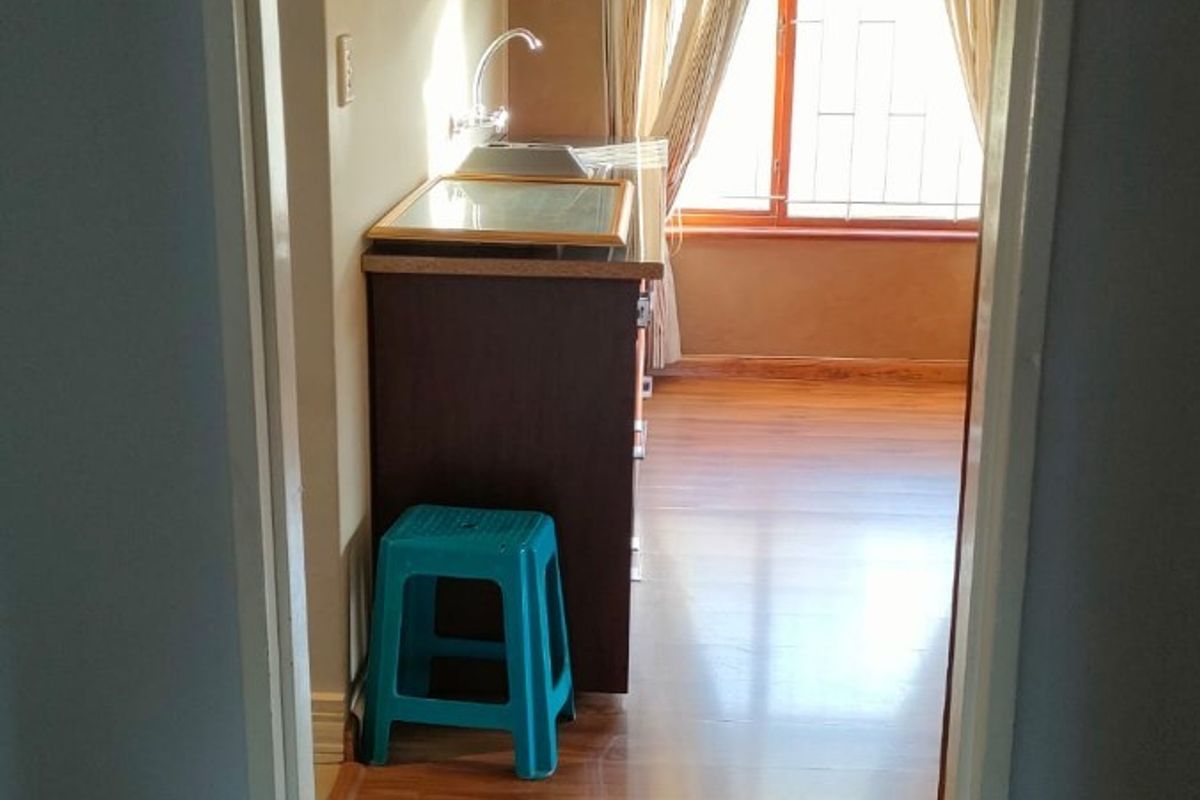 A compact kitchen area featuring laminate flooring, built-in cabinetry, and a sink, viewed through a doorway.