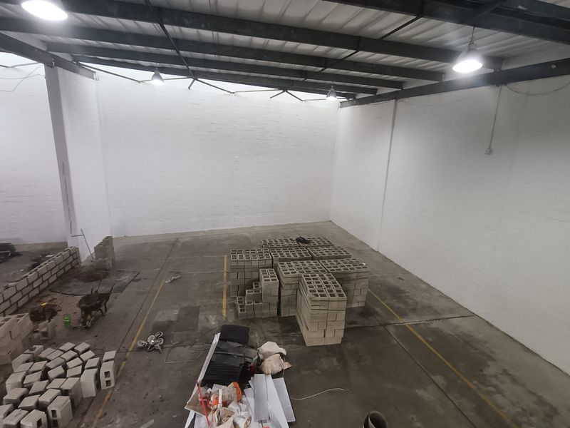 Spacious industrial utility area featuring high ceilings with exposed steel trusses, painted masonry walls, and durable concrete flooring, suitable for storage or workshop use.