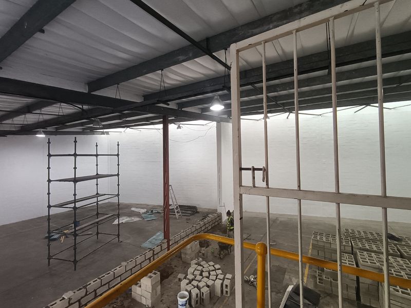 Spacious industrial warehouse interior featuring high exposed steel ceilings, painted brick walls, and concrete flooring, currently undergoing renovation.