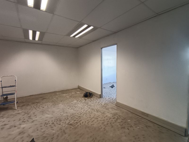 An empty office space featuring a suspended ceiling with recessed lighting and unfinished concrete flooring, ready for final floor finishes.