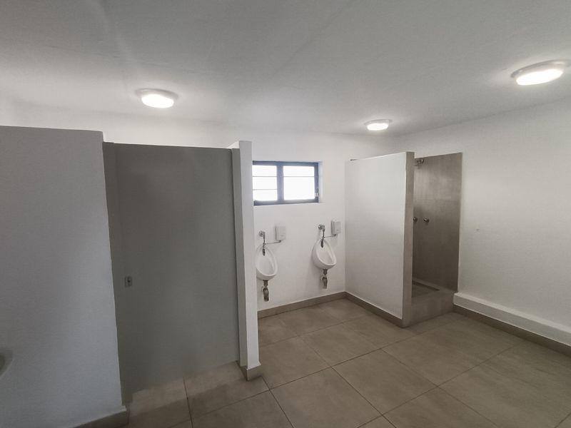 Industrial-style communal bathroom featuring tiled flooring, multiple urinals, and a dedicated shower cubicle with partition walls.