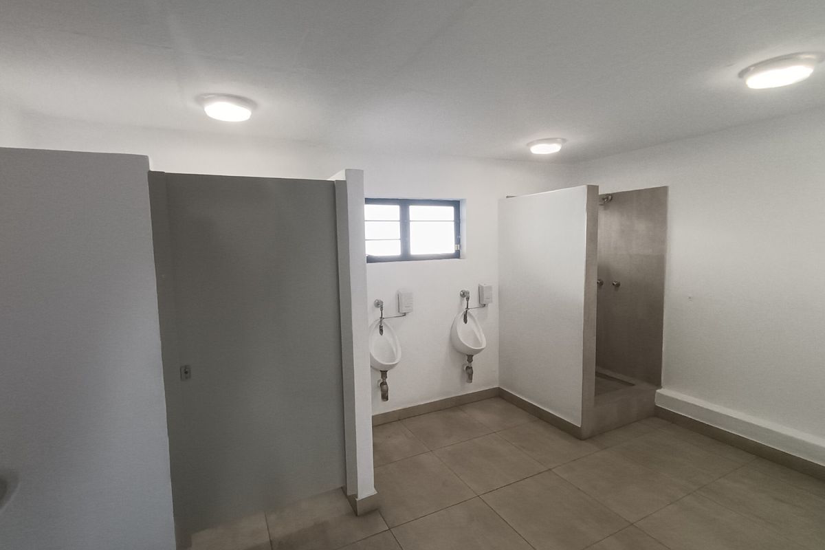 Industrial-style communal bathroom featuring tiled flooring, multiple urinals, and a dedicated shower cubicle with partition walls.