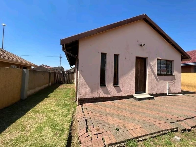Rear view of the property featuring a paved patio area, perimeter wall, and exterior wall finishes requiring maintenance.