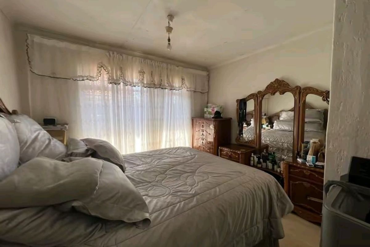 A bedroom featuring a large window with curtains and visible signs of wear on the ceiling and wall finishes.