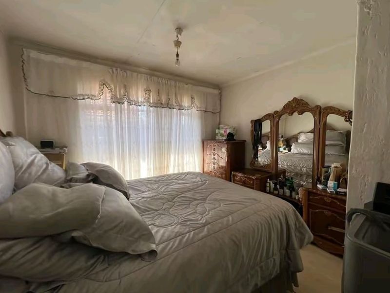 A bedroom featuring a large window with curtains and visible signs of wear on the ceiling and wall finishes.