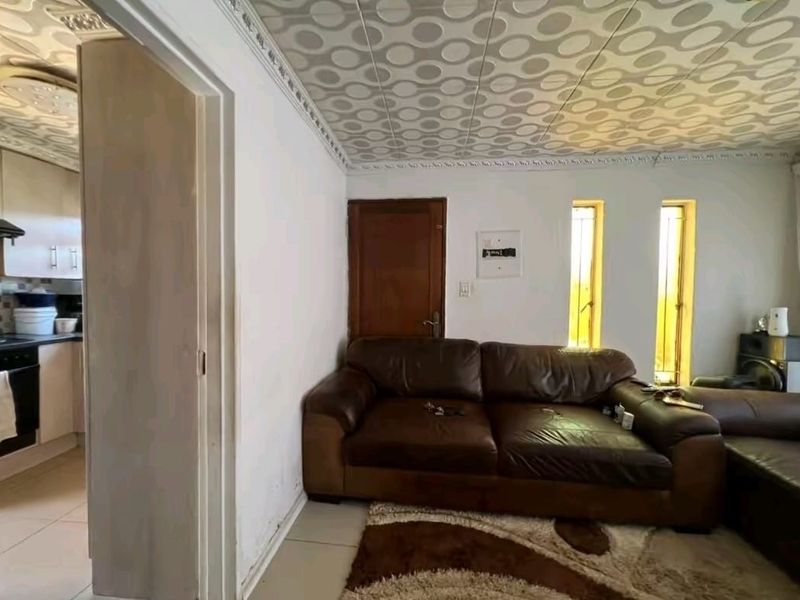 Open plan living area featuring tiled floors and a distinctive patterned ceiling, with an adjacent kitchen area visible through the doorway.
