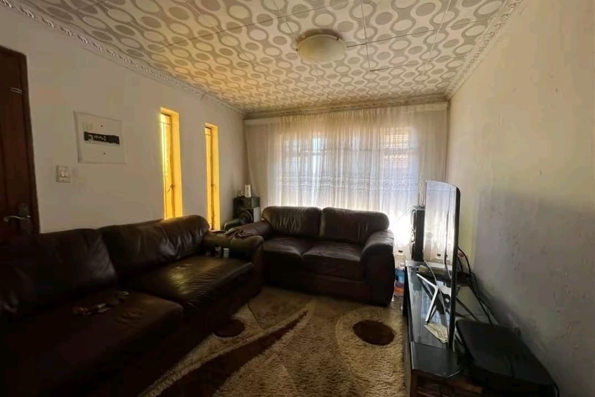 A living room featuring a distinct patterned ceiling, vertical accent windows, and a large window with curtains, requiring cosmetic updates to modernize the space.