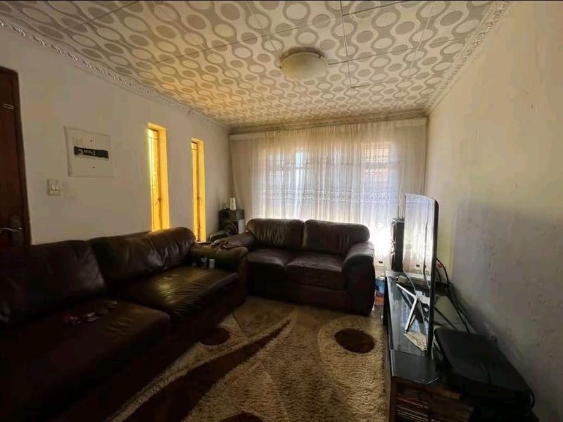 A living room featuring a distinct patterned ceiling, vertical accent windows, and a large window with curtains, requiring cosmetic updates to modernize the space.