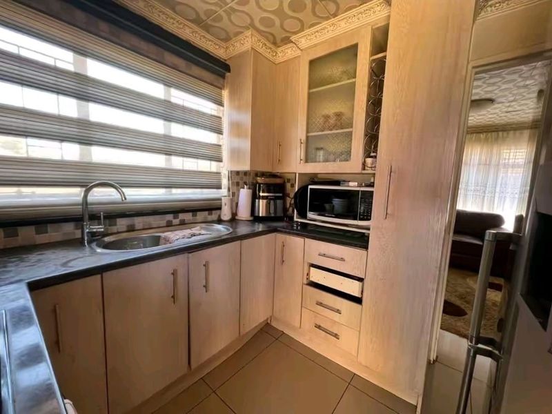 A functional kitchen featuring light wood-tone cabinetry, dark laminate countertops, a stainless steel sink, and mosaic tile backsplash with tiled flooring.