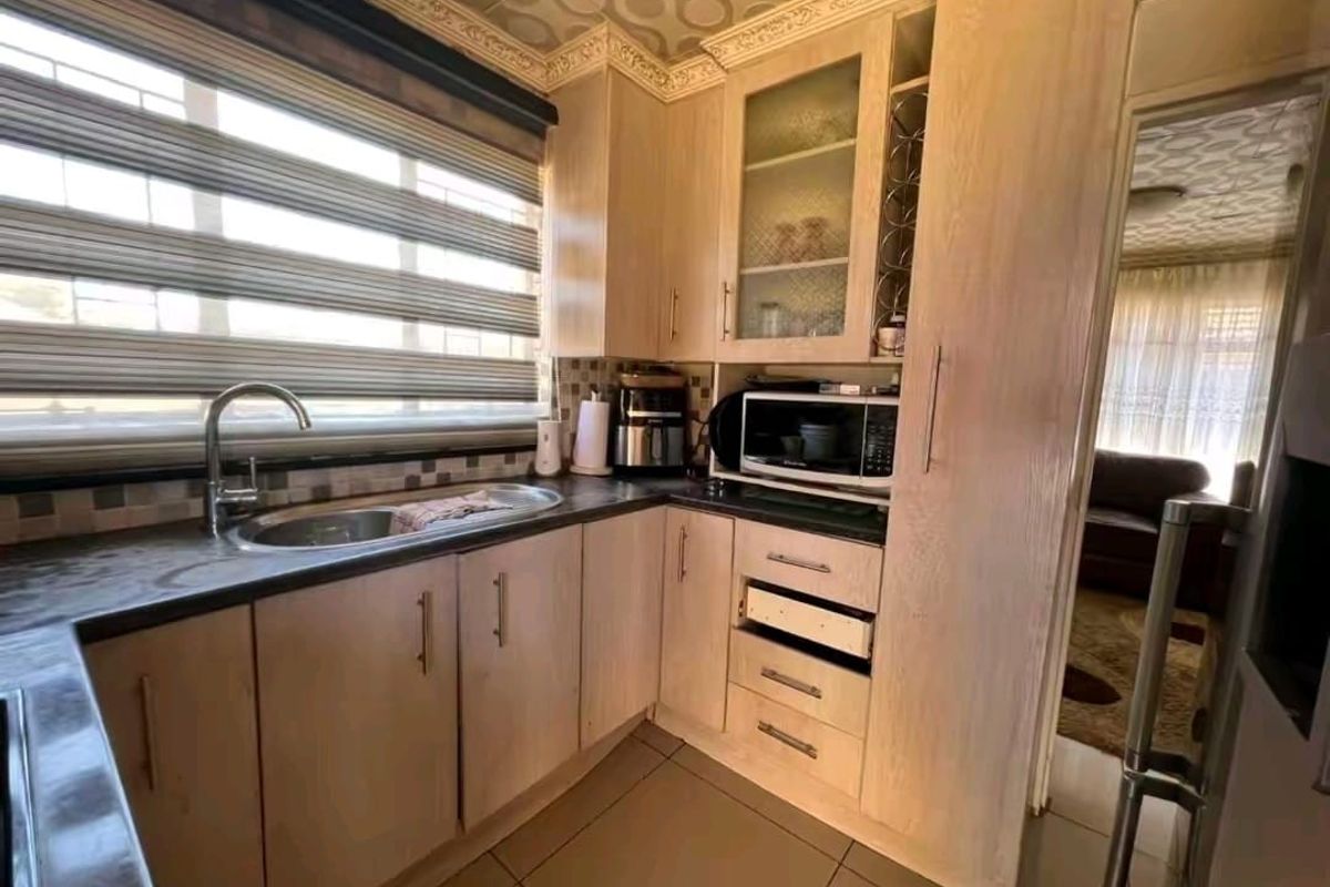 A functional kitchen featuring light wood-tone cabinetry, dark laminate countertops, a stainless steel sink, and mosaic tile backsplash with tiled flooring.