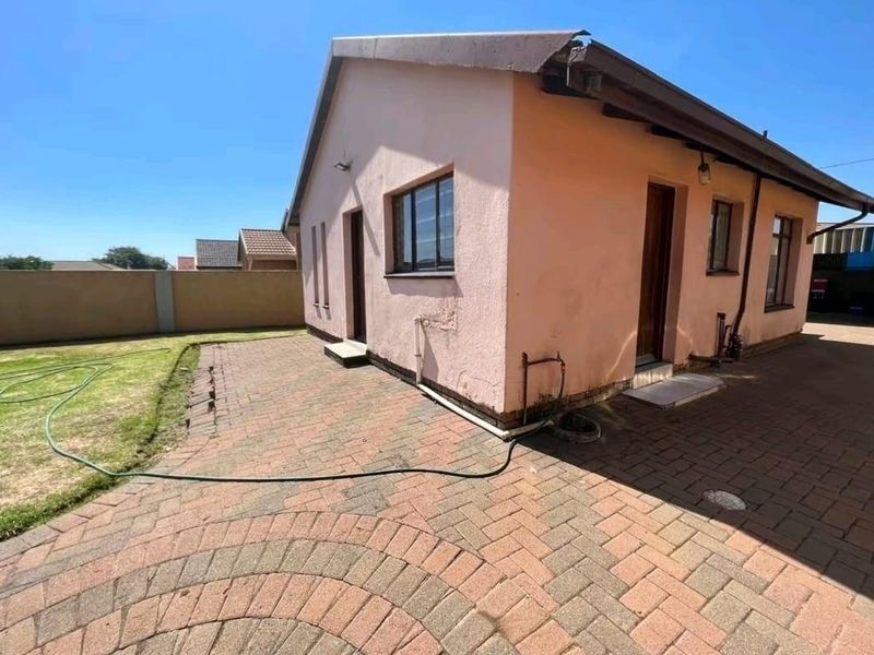 Rear exterior view of the property featuring a paved patio area, perimeter wall, and access points to the building.
