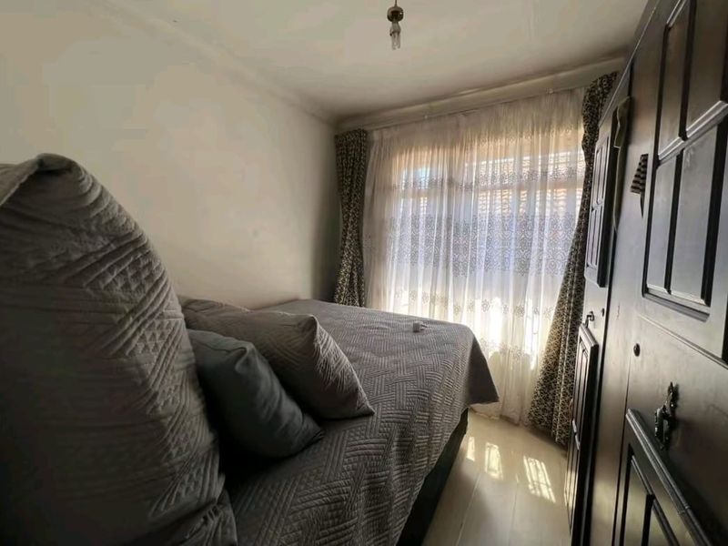 A compact bedroom featuring a built-in wardrobe and natural light through a window with curtains.