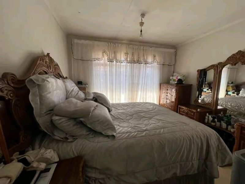 A bedroom featuring a window with curtains, showing signs of wear including ceiling cracks and peeling paint, suitable for renovation.