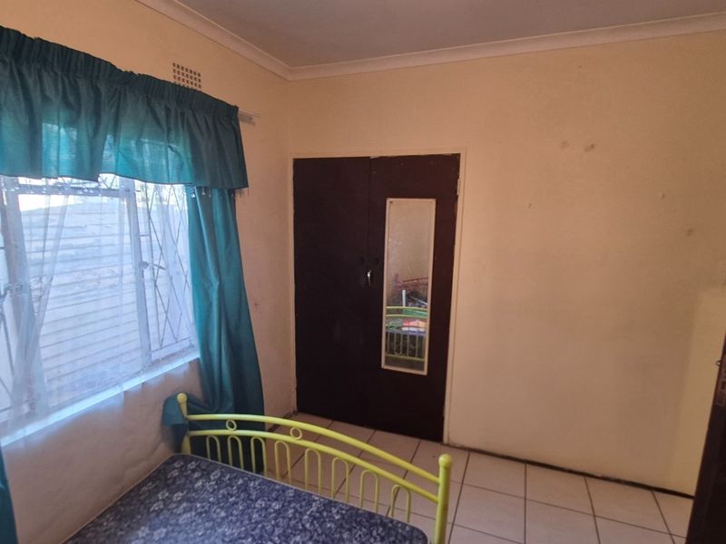 A bedroom featuring tiled flooring, a built-in wardrobe with a mirror, and security bars on the window.