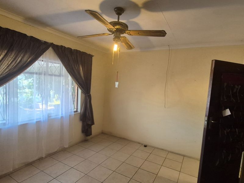 A vacant bedroom featuring tiled flooring, a ceiling fan, and security bars on the window, requiring minor cosmetic updates.