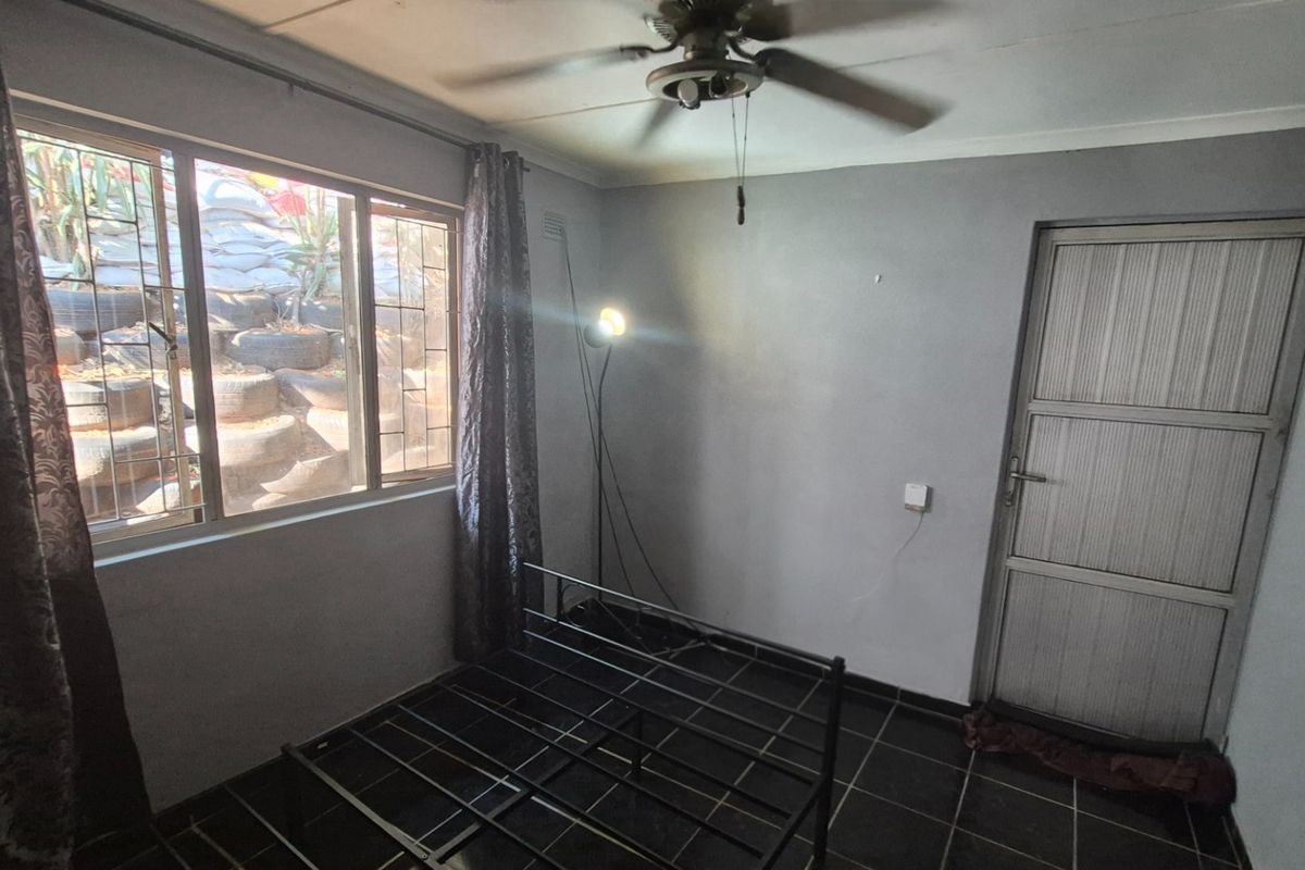 A simple bedroom featuring tiled flooring, a ceiling fan, and an exterior door, offering a blank canvas for potential renovation or staging.