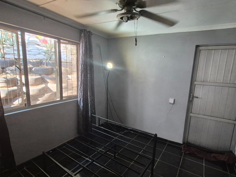 A simple bedroom featuring tiled flooring, a ceiling fan, and an exterior door, offering a blank canvas for potential renovation or staging.