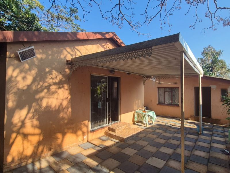 Rear exterior view featuring a covered patio area with tiled flooring, sliding door access, and a metal roof awning.