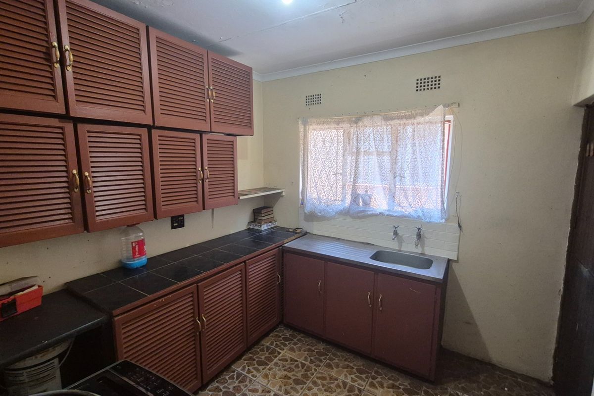 A dated kitchen featuring louvered wooden cabinetry, tiled countertops, and a stainless steel sink, offering significant potential for modernization and renovation.
