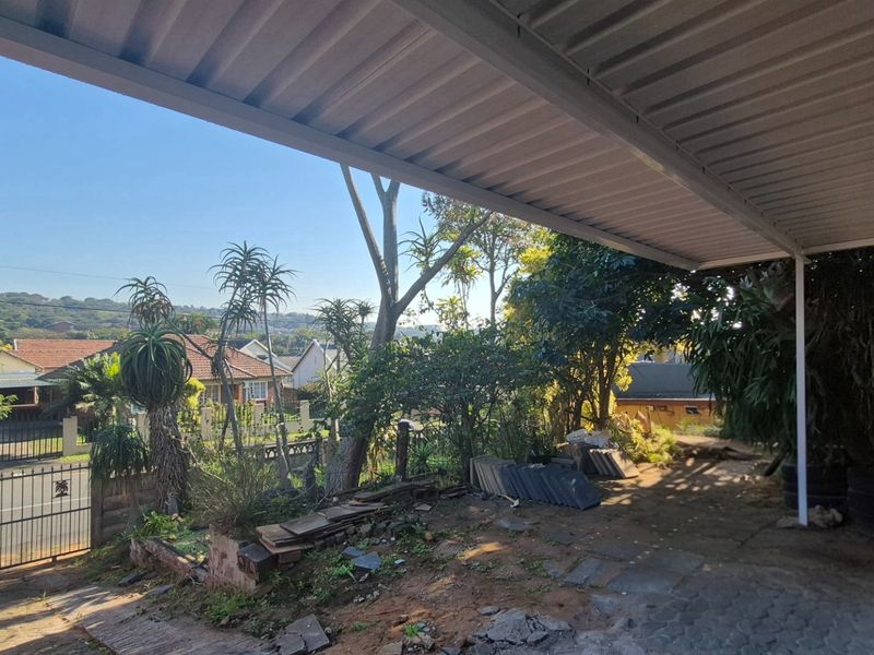 Covered outdoor patio area with metal roofing, overlooking a residential street and garden, requiring landscaping and surface improvements.