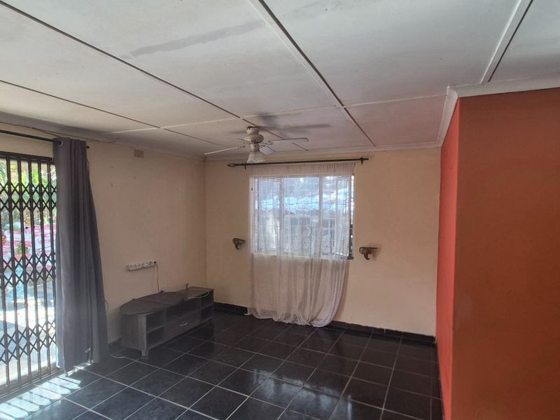 A spacious living area featuring dark tiled flooring, a ceiling fan, and a sliding glass door with a security gate leading to the exterior.