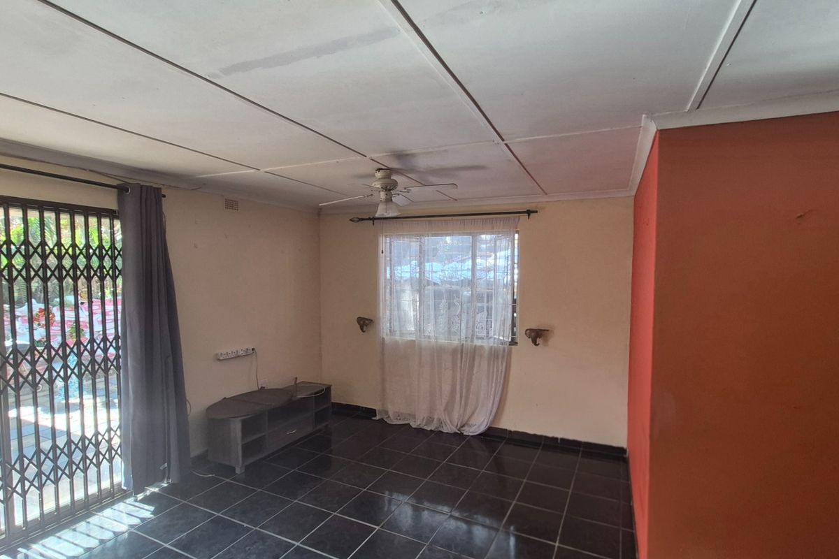 A spacious living area featuring dark tiled flooring, a ceiling fan, and a sliding glass door with a security gate leading to the exterior.
