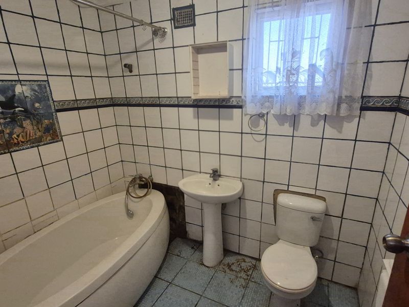 A dated bathroom featuring a pedestal basin, toilet, and bathtub with decorative wall tiling. The space requires renovation to update finishes and improve condition.