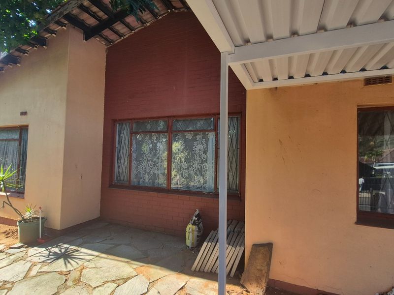 Rear exterior view of the house featuring a stone paved patio area, a metal carport structure, and brick facade with steel frame windows.