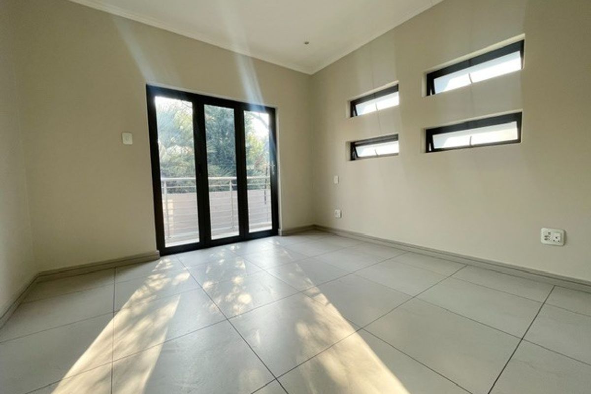 A bright, empty bedroom featuring large aluminium sliding doors leading to a balcony and modern horizontal clerestory windows with neutral tiled flooring.