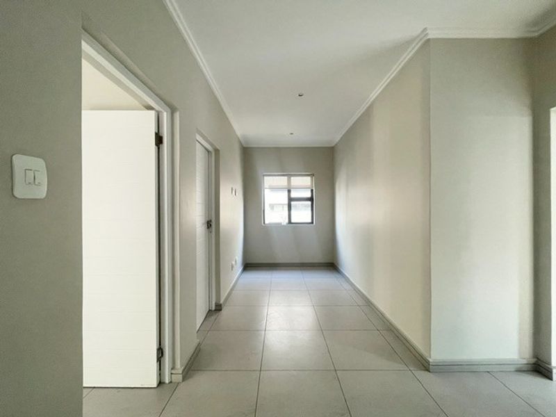 A clean, well-lit hallway featuring neutral tiled flooring, modern cornicing, and recessed downlights, providing a bright and spacious transition between rooms.