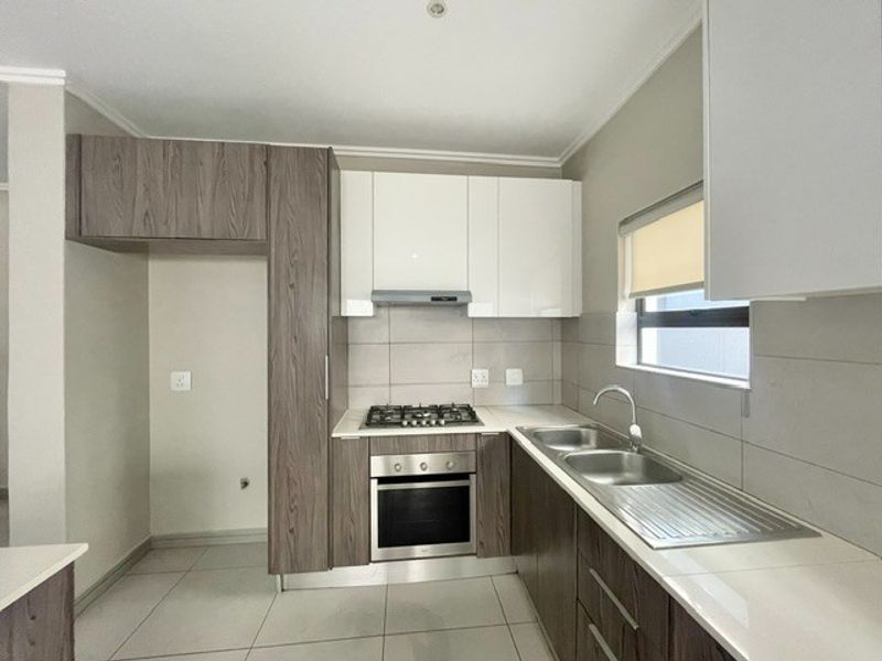 Modern kitchen featuring two-tone cabinetry, stone countertops, built-in gas hob, electric oven, extractor fan, and a double sink with tiled splashback.