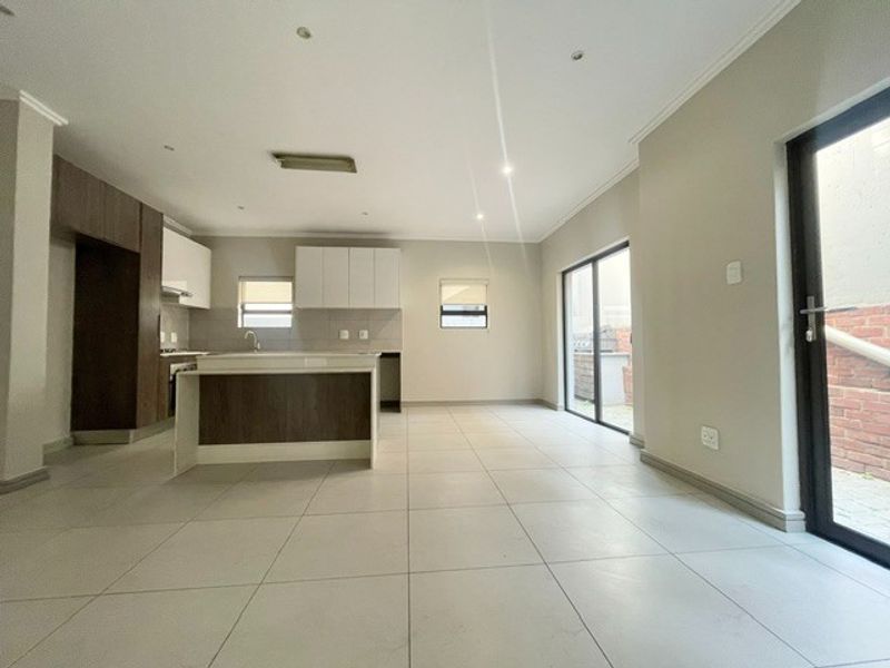 Spacious open-plan kitchen and living area featuring modern cabinetry, a central island, tiled flooring, and direct access to the outdoor space through sliding doors.