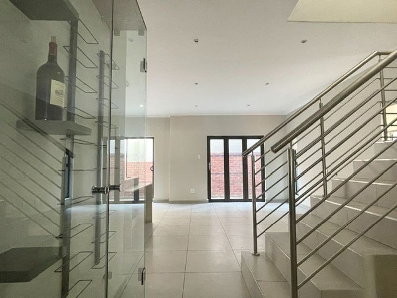 Spacious open-plan living area featuring tiled floors, a modern stainless steel staircase, and a built-in glass wine display cabinet leading to rear patio doors.